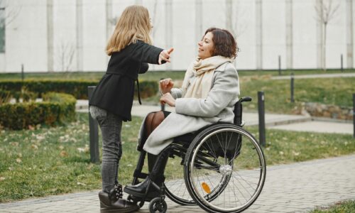 child smiling at mother who is in a wheelchair sat outdoors on path